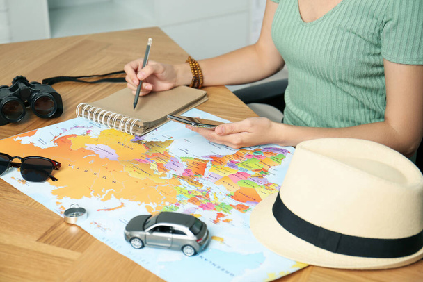 Woman with world map and smartphone planning trip at wooden table, closeup - Φωτογραφία, εικόνα