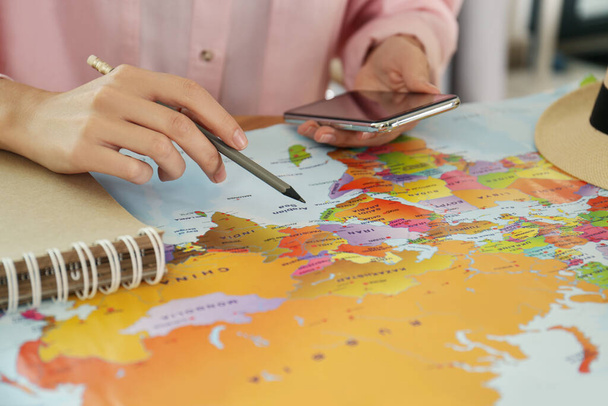 Woman with world map and smartphone planning trip at table, closeup - Фото, изображение