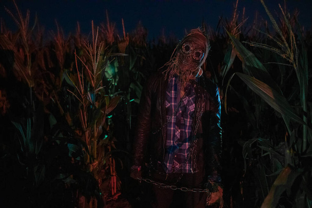Chodící mrtvá zombie stojí v noci na kraji kukuřičného pole s kovovým řetězem v ruce.. - Fotografie, Obrázek