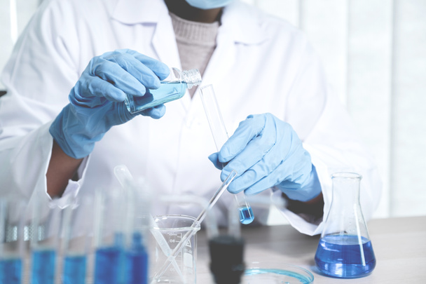Los científicos sostienen un tubo de vidrio lleno de líquido químico azul para investigación y análisis en un laboratorio. - Foto, imagen
