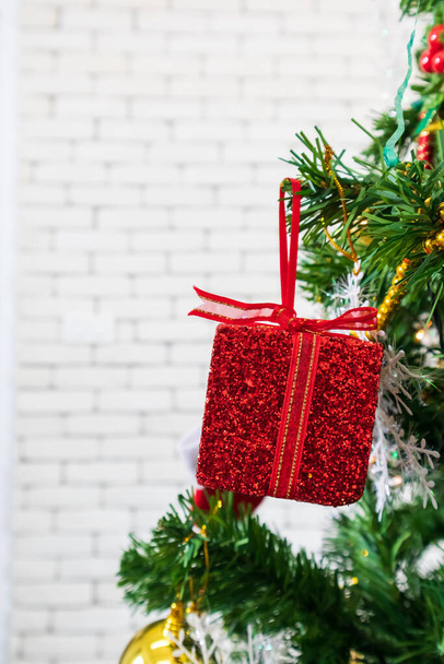 Χριστουγεννιάτικο δέντρο διακοσμημένο με κόκκινο κουτί δώρου σε λευκό τοίχο, αντίγραφο χώρου. - Φωτογραφία, εικόνα