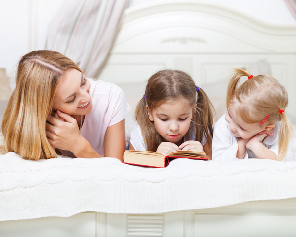 Madre y sus hijas leyendo libro de cuentos a la hora de dormir
 - Foto, Imagen