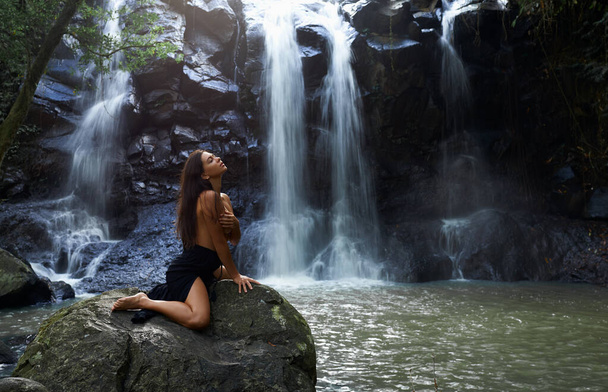 красива дівчина сидить на фоні водоспаду на камені
 - Фото, зображення
