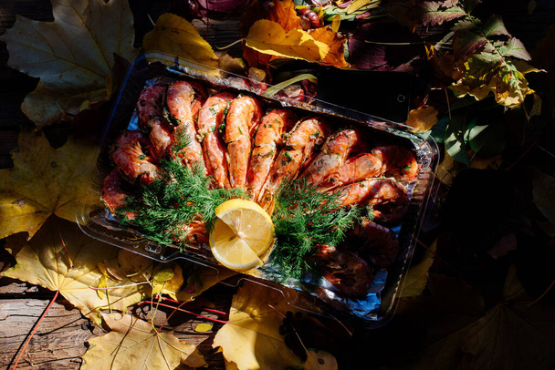 Fried shrimps with lemon and dill on wooden table with autumn leaves, mushrooms and chestnuts. - Foto, imagen