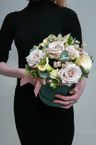 Bouquet of flowers in green hat box in the hands of a woman florist on a light background. Rosa, calla, astrantia, eucalyptus, ozotamnus. - Zdjęcie, obraz