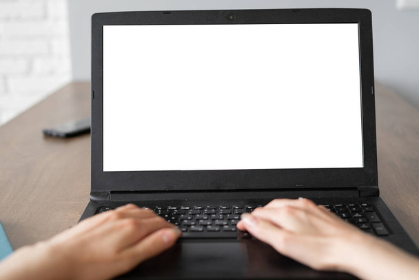 Laptop z pustym ekranem na białym stole z rozmytym tłem jako koncepcja. dwie ręce wpisują tekst na klawiaturze. - Zdjęcie, obraz