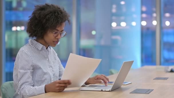 Εστιασμένη Αφρικανή επιχειρηματίας με έγγραφα ανάγνωσης laptop στο γραφείο  - Πλάνα, βίντεο