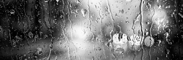 Панорамне зображення. Розмиті автомобільні вогні чорно-білого кольору. Краплі дощу на передньому вікні
 - Фото, зображення