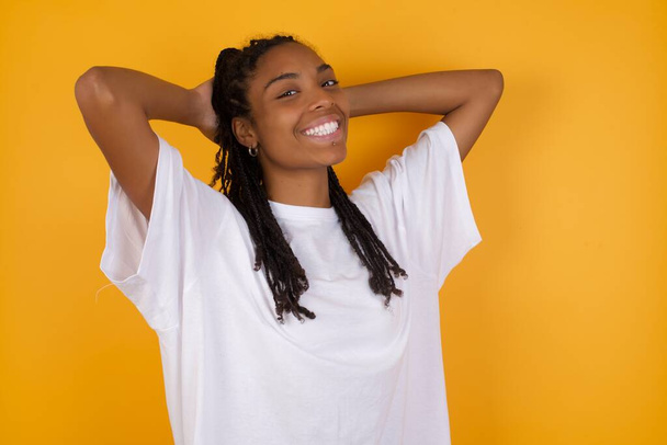 смеющаяся африканская американка на жёлтом фоне и держащаяся за руки за голову  - Фото, изображение