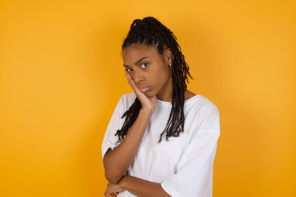 Грустная африканская американка держит руку на щеке на желтом фоне  - Фото, изображение