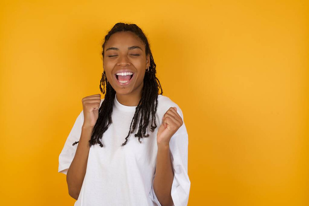 nevetés afro-amerikai nő sárga háttér, csukott szemmel  - Fotó, kép