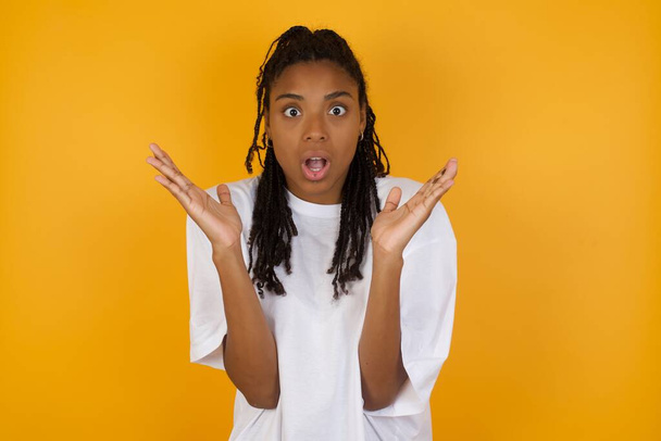 shocked african american woman against yellow background, gesturing with hands  - Photo, Image