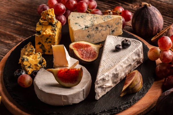 Finom ínyenc sajt, lágy sajtok választéka szeletelt édes friss fügével és szőlővel, rusztikus fából készült háttérrel, élelmiszer recept háttér. Közelről.. - Fotó, kép