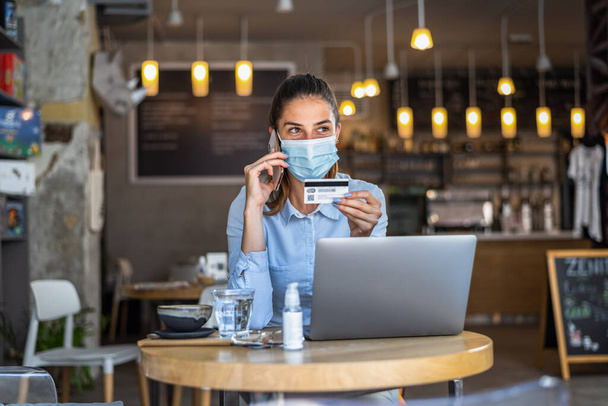 Portrait of young business woman wearing mask while doing shopping online and payment by credit cards. Conceptual of new normal lifestyle during covid-19 pandemic. - Photo, image