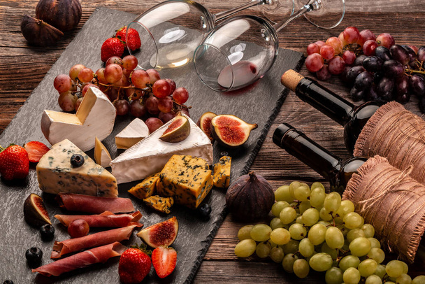 still life, food composition with assorted cheese, glass of wine and fruits on a wooden table. - Photo, image