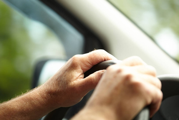 Driver's hands. Male hands on the steering wheel while driving a car. Selective focus of male hands on the steering wheel on a sunny day. Car driving. Transport, vacation, travel and automotive concept. - Photo, image