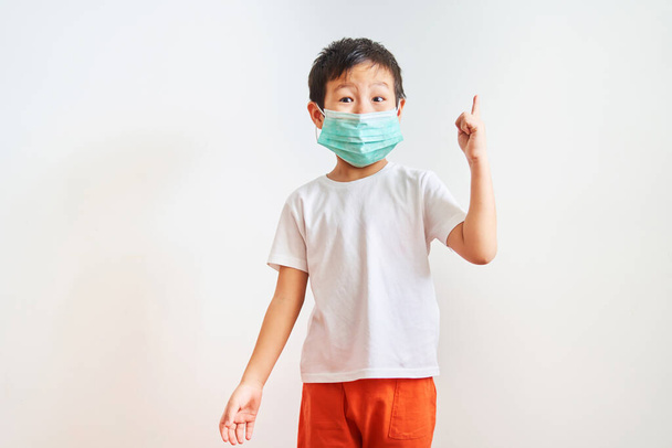 Asian child stands in green medical mask, raised his index finger up - child on a white background, has an idea                                - Foto, Imagem