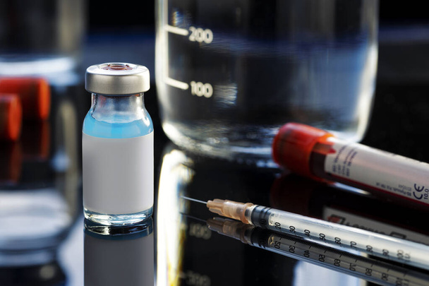 Vaccine bottle with a blue liquid, a syringe and a blood sample on a laboratory like background. - Zdjęcie, obraz