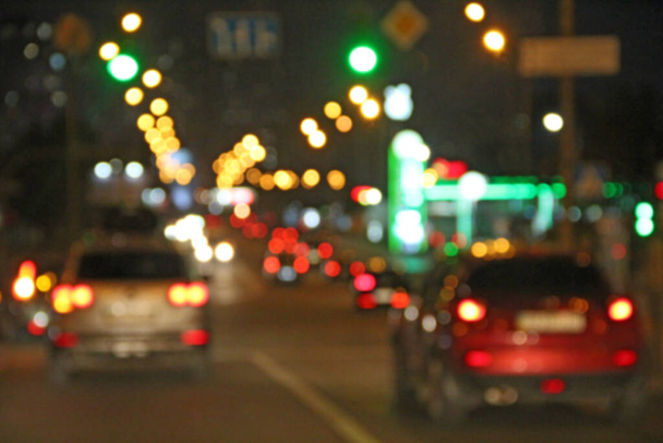 Avtomobiles con faros y luces encendidas en la ciudad nocturna. Coches con faros encendidos. Señal de luces de transporte. Línea de coches en la carretera. Imagen borrosa - Foto, Imagen