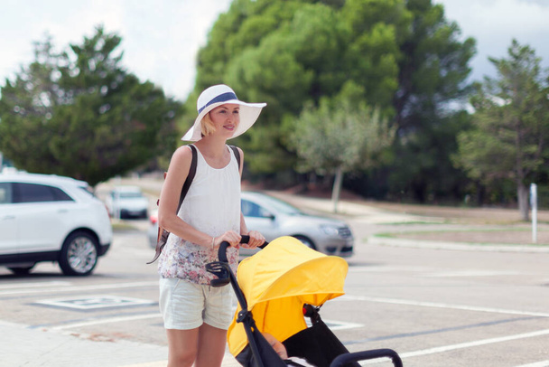 Young mother pushing stroller with sleeping baby outdoors - Photo, Image