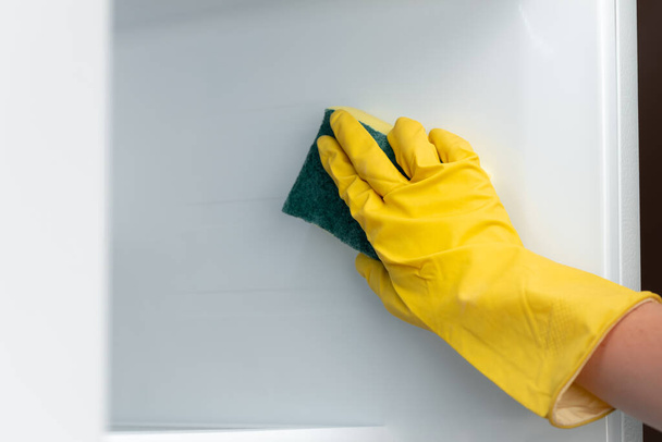 Hand of a woman in yellow glove cleaning the fridge shelf - Fotó, kép