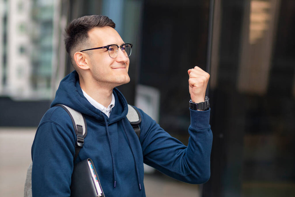 Happy positive successful college student, cheerful pupil, young handsome man with book smiling in glasses, looking at result list. Smart boy passed university exam, test, celebrating victory, triumph - Fotoğraf, Görsel