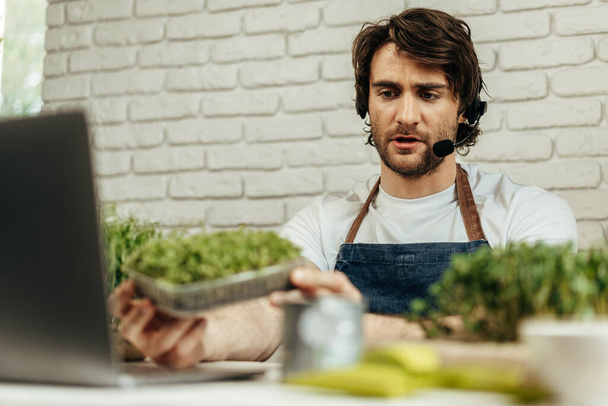 Handsome bearded man sells plant sprouts and seedlings online using laptop - 写真・画像