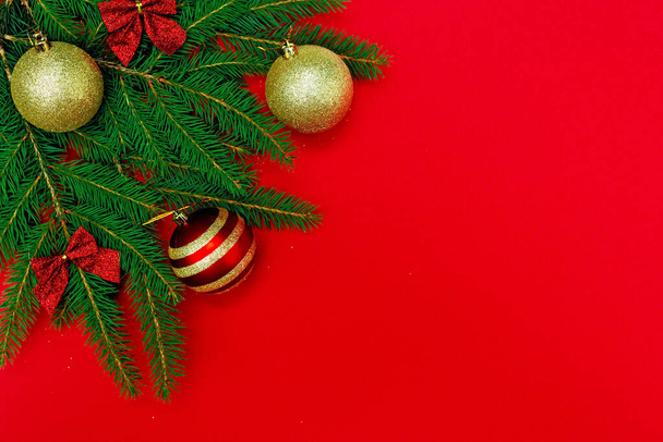 Composizione natalizia minima. I rami dell'albero di Natale sono decorati con palline d'oro e un fiocco, isolato su uno sfondo rosso. Concetto di Capodanno. Copia spazio. - Foto, immagini