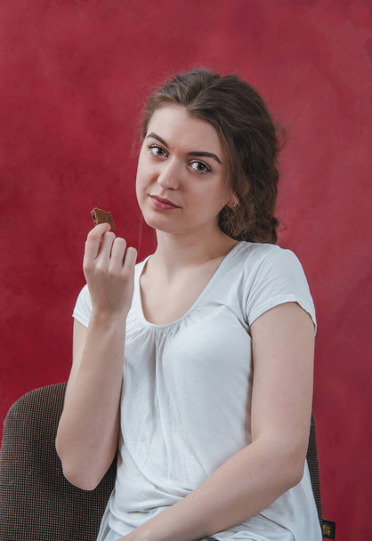 Pretty girl eating chocolate. Portrait on red background, delicious food, sweet chocolate. - Fotografie, Obrázek