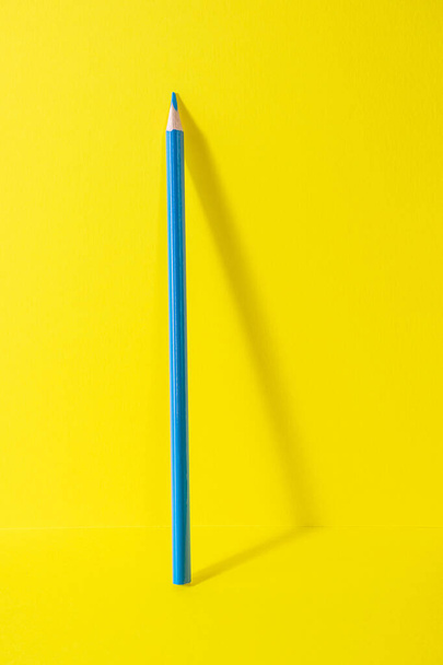 Wracać do szkoły. Niebieski ołówek stoi na żółtym tle. Kreatywna minimalistyczna koncepcja kreatywności dzieci, rysunek. - Zdjęcie, obraz