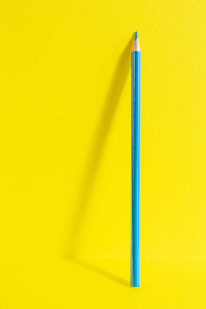 Torniamo a scuola. Una matita blu poggia su uno sfondo giallo. Concetto minimalista creativo di creatività da bambini, disegno. - Foto, immagini