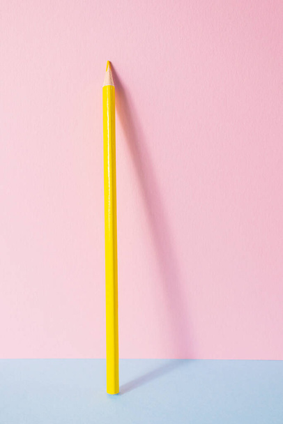 Πίσω στο σχολείο. Ένα κίτρινο μολύβι στέκεται σε ροζ-μπλε φόντο. Δημιουργική μινιμαλιστική έννοια της παιδικής δημιουργικότητας, σχέδιο. - Φωτογραφία, εικόνα