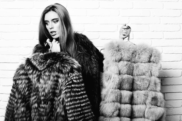 surprised fashionable woman in fur on white brick wall studio background - 写真・画像