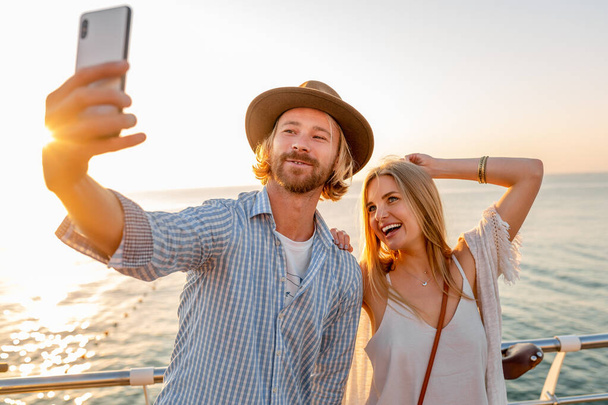 young attractive smiling happy man and woman traveling on bicycles taking selfie photo on phone camera, romantic couple by the sea on sunset, boho hipster style outfit, friends having fun together - Foto, immagini