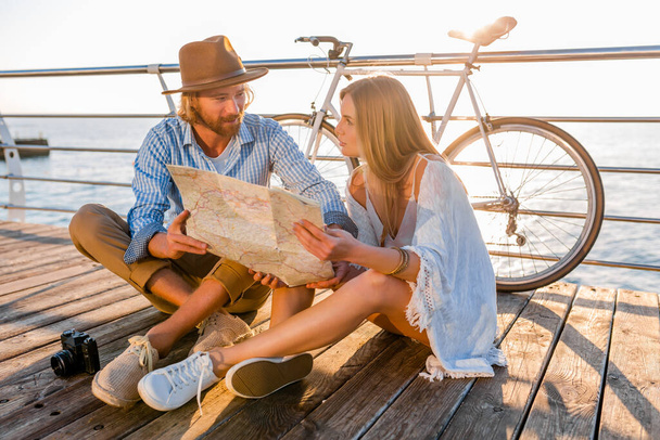 attractive happy smiling couple traveling in summer by sea on bicycles, man and woman with blond hair boho hipster style fashion having fun together, looking in map sightseeing - Foto, imagen