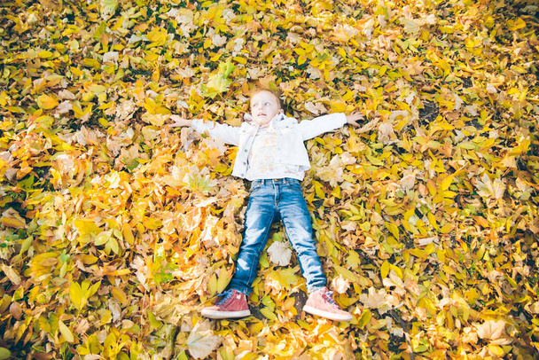 μικρό κοριτσάκι ξαπλωμένο στο έδαφος σε κίτρινα φύλλα φθινοπωρινή εποχή - Φωτογραφία, εικόνα