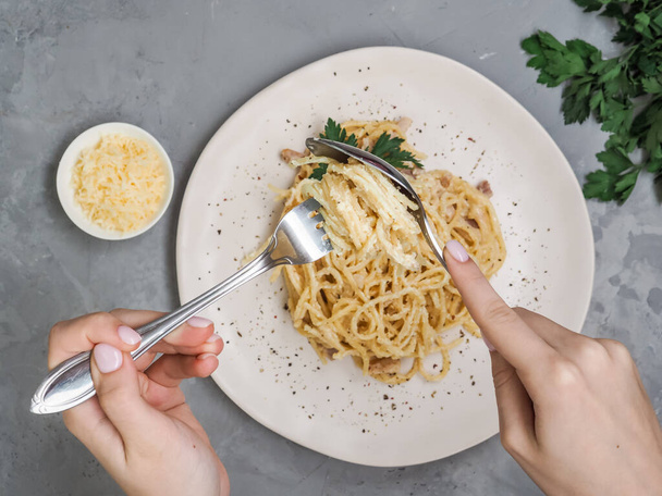 Kadınlar maydanozlu, gevrek pastırmalı, peynirli ve sarımsaklı ev yapımı carbonara yiyorlar. İtalyan görgü kurallarına uygun olarak spagettiyi sarmak için eller kaşık çatalını çevirir. - Fotoğraf, Görsel