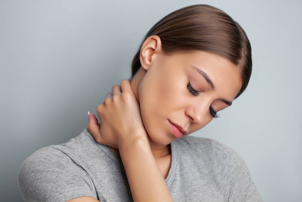 Молодая женщина испытывает сильную боль в шее, держа руки - Фото, изображение