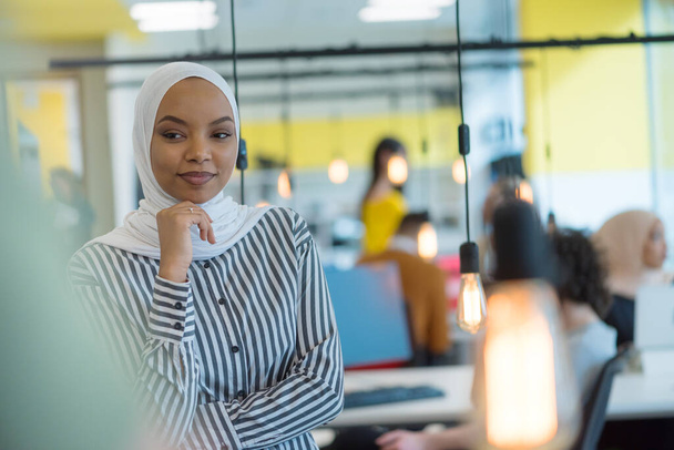 Moslim zakenvrouw draagt hijab en werkt op de computer in het kantoor. Mooie Afrikaanse vrouw in hijab die naar de camera kijkt en glimlacht. Begrip werkplek en multi-etnische relaties - Foto, afbeelding