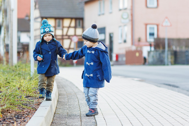Два маленьких сидящих мальчика, идущих по улице в немецкой деревне
. - Фото, изображение