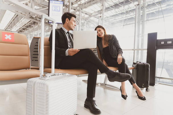 Egy utas üzletember és egy nő boldogan beszél, miközben a reptéren várják a beszállást csomagokkal a közelben, életmód üzletemberek..  - Fotó, kép
