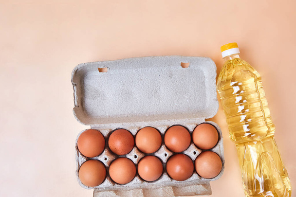 10 eggs in a cardboard egg box and a bottle of sunflower oil on a light, simple table. Brown fresh eggs cooking concept, in the kitchen, grocery store, close-up isolated - Photo, Image