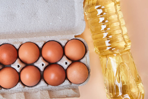 8 eggs in a cardboard egg box and a bottle of sunflower oil on a light, simple table. Brown fresh eggs cooking concept, in the kitchen, grocery store, close-up isolated - Photo, Image