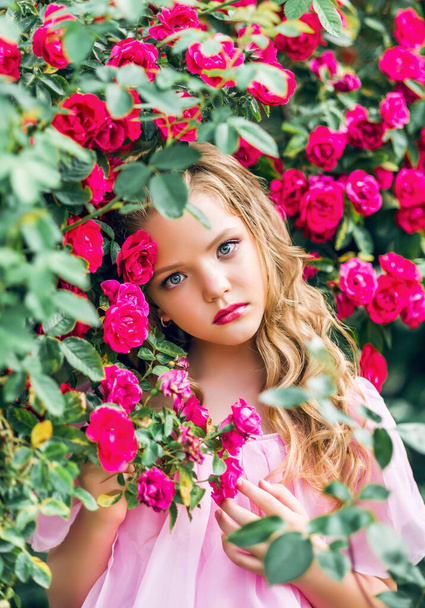 girl in pink dress in a lush garden amid roses - Photo, Image