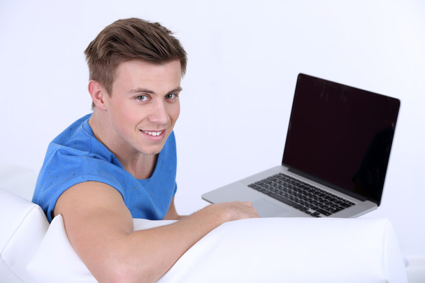 Guy sitting on sofa with laptop on white background - Fotó, kép