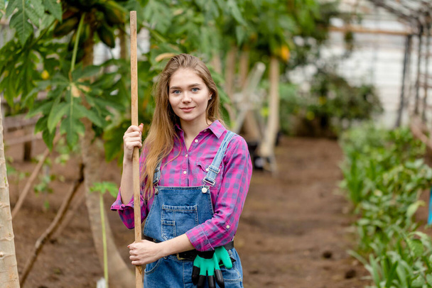 Woman wearing jeans and shirt in her garden posing with a shovel - Foto, afbeelding