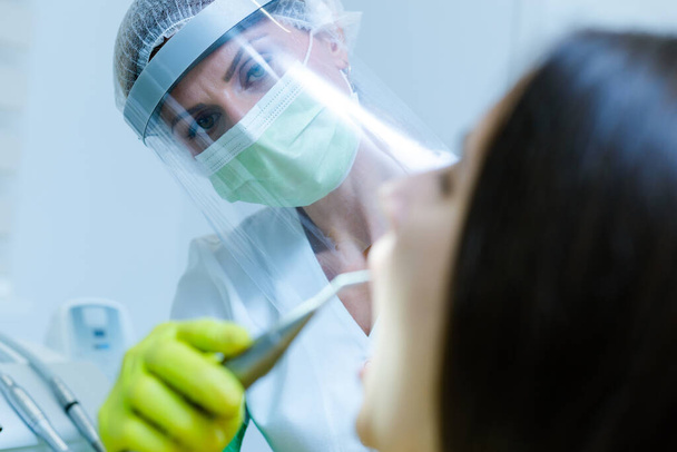 Coronavirus güvenlik önlemi olarak yüz maskesi, eldiven ve güneşlik takan kadın diş hekimi. - Fotoğraf, Görsel