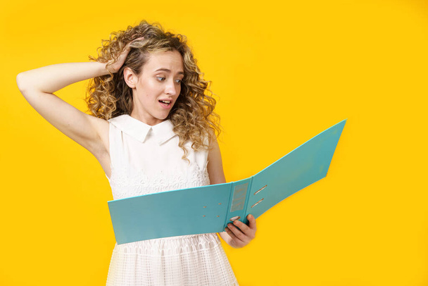 A young woman holds folders with documents in her hands. Reads and wonders. Isolated on yellow background - Фото, изображение