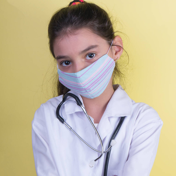 Mała zabawna dziewczynka z kolorowym stetoskopem w mundurze doktora. kolorowa maska, panorama. przestrzeń do kopiowania. Portret małego lekarza. Zawieszony 19. rękawice rozpylające  - Zdjęcie, obraz