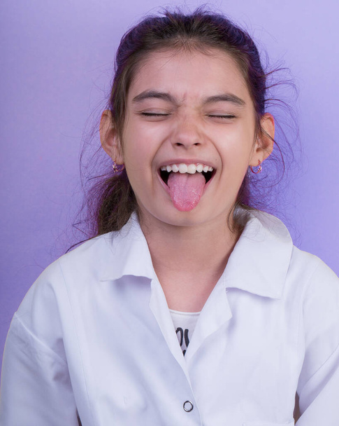 Little funny girl with a collorful stethoscope while wearing Doctor's uniform. Excitement and fascination concept. Coronavirus background. foolish grimaces comical crazy gestur.  Funny expression.  - Photo, Image